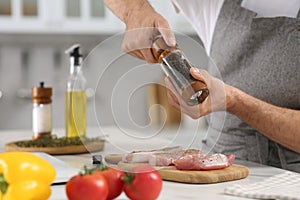 Man peppering steak at table in kitchen, closeup. Online cooking course