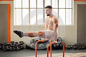 Man performing L sit on parallel bars calisthenics exercise in fitness club