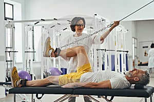 Man performing a leg exercise supervised by a kinesiologist