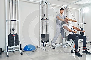 Man performing seated straight-arm pulldown aided by kinesiologist