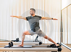 Man performing a Warrior 2 yoga pose on a pilates reformer bed