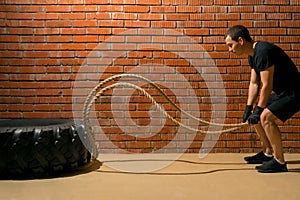 Man performs an endurance exercise with ropes on a brick wall background