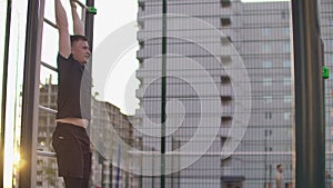 A man performs a leg lift on parallel bars in slow motion against the background of buildings in a city Park