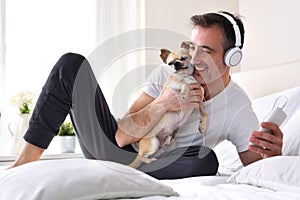 Man petting his chihuahua dog listening to music on bed