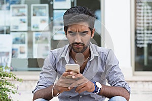 Man phone. Closeup portrait angry indian male holding texting looking at cellphone isolated outdoors background