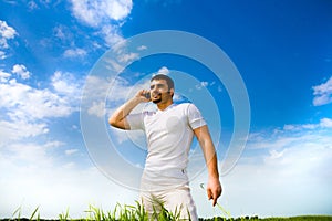 Man at the phone in the field under blue sky