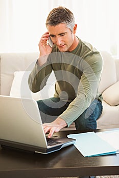 Man on the phone sitting on the couch and using laptop
