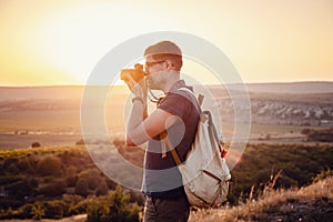 Man photographer with backpack and camera taking photo of sunset mountains
