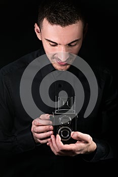 Man photographer holding a camera. Shooting process. Retro photo camera medium format twin-lens reflex camera on a black