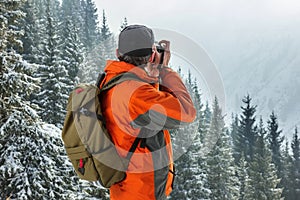 A man photographes a winter landscape. Against the background of mountains and pines