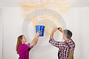 Man Photographing While Woman Collecting Water From Ceiling