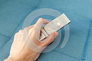 Man picking up holding a modern silver smart TV remote in his hand on a couch, sofa watching television, online video streaming