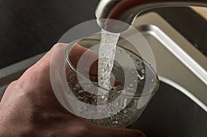 A man picks up drinking water in a glass from under the kitchen faucet