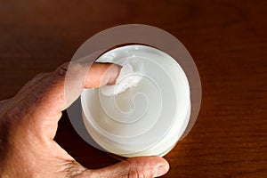 A man picks up white Vaseline to moisturize his skin, dark background