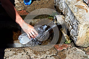 Man picks water in plastic bottle from natural source that pours from iron pipe