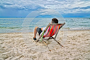 Man picnicking and overlooking the sea sitting on a red chair at the beach