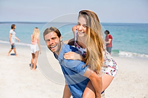 Man piggybacking girlfriend against friends at beach