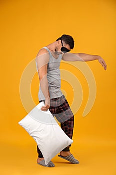 Man with pillow and eye mask in sleepwalking state on yellow background