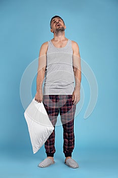 Man with pillow in sleepwalking state on light blue background