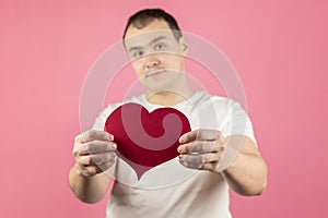Man on a pink background holds out a red paper heart in the camera