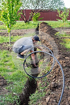 A man places a plastic pipe on top of a dug ditch to supply water to a drip irrigation system and buries it