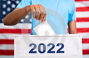 Man placing ballot paper into 2022 ballot box in front of american flag - concept of 2022 midterm US election, voting photo