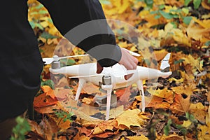 Man placing white drone in yellow autumn leaves