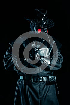 Man in plague doctor costume with crow-like mask praying with hands isolated on black background. Creepy mask photo