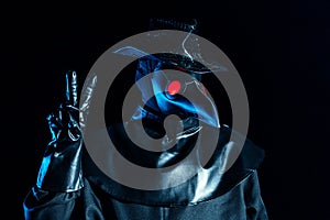Man in plague doctor costume with crow-like mask showing peace gesture isolated on black background. Creepy mask photo