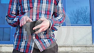 A man in a plaid blue red shirt takes out a wallet, opens it and looks inside.