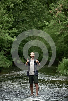 A man in a plaid shirt with a backpack crosses the river