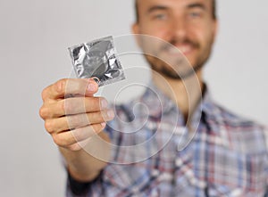 Man in plaid shirt holds a new condom in hand and smile, concept