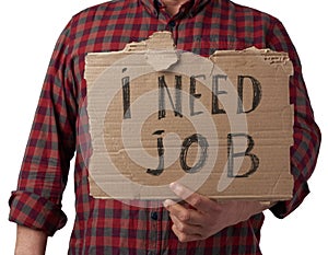 Man in a plaid shirt and jeans holds a piece of paper with the inscription i need job