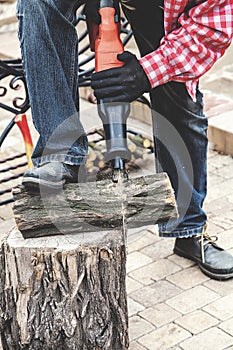 Man in plaid shirt sawing piece of wood on stump