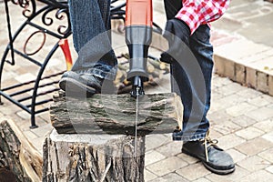 Man in plaid shirt sawing piece of wood on stump