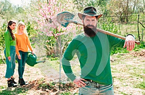 Man plants a tree, hands with shovel. Group of youth work in spring yard with garden tools. Friends plants and grows