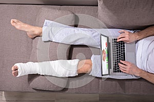 Man With Plastered Leg Using Laptop