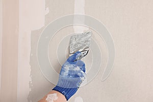Man plastering wall with putty knife indoors, closeup. Home renovation