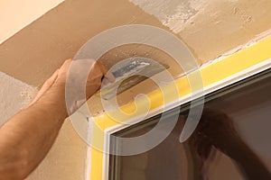 Man plastering window area with putty knife indoors. Interior repair