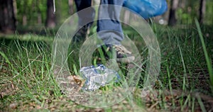 A man with a plastic bag collects garbage in the forest by impaling it on a stick