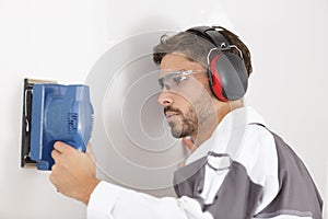 man with plastic glasses sanding wall