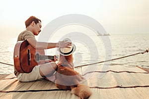 A man play guitar music song near the sea sunset and try wearing hat in dog head