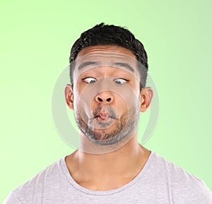 Man, play and silly in studio, face and goofy comic or funny expression on green background. Male person, mockup space