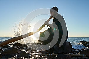 Man playing on Austaralian didjireedoo insturment in sunshine at seashore