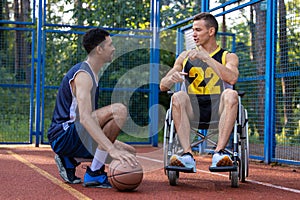 Man playing basketball with disabled friend in wheelchair at outdoor court.