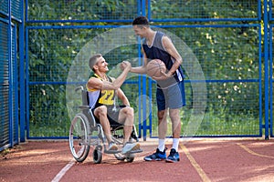 Man playing basketball with disabled friend in wheelchair at outdoor court.