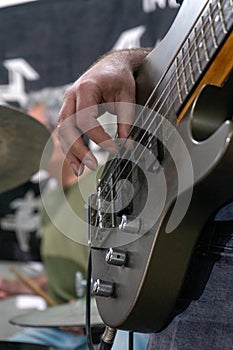 A man playing a bass guitar in a casual setting. He\'s focused on his instrument, fingers gliding over the strings.