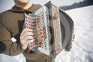 Man is playing on beautiful old harmonica accordion in winter nature