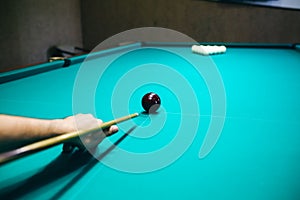 Man is playing billiard. Guy is holding pool cue in his hand. Small black cue ball is on the centre of the green table. Sports and