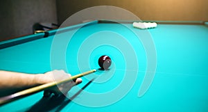 Man is playing billiard. Guy is holding pool cue in his hand. Small black cue ball is on the centre of the green table. Sports and